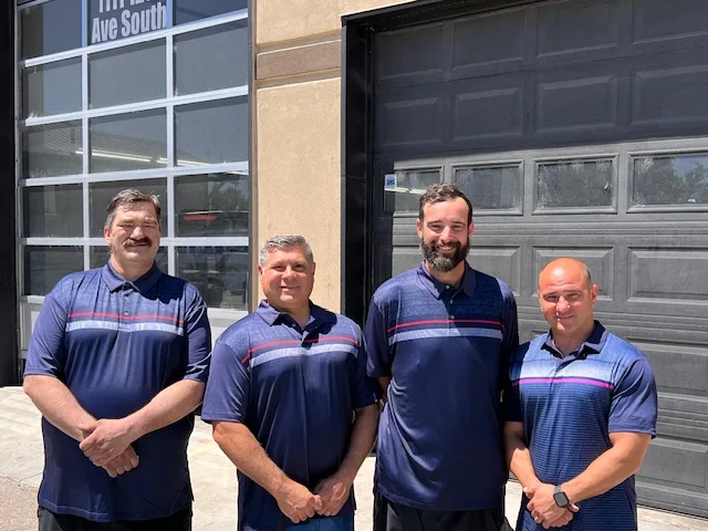 The image shows the team members of Nampa Total Car Care in front of their auto repair shop located at 1111 12th Ave S, Nampa, ID.