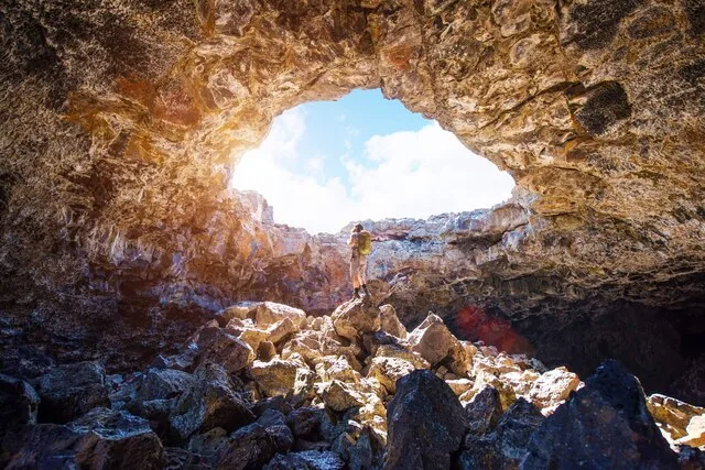A hiker exploring a lava cave at Craters of the Moon National Monument in Idaho.