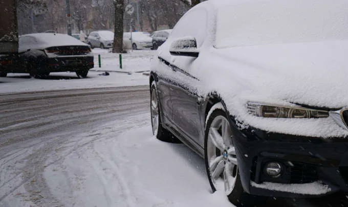 Car covered in snow parked on a winter road in Nampa ID, showing the need for seasonal auto repair and maintenance.